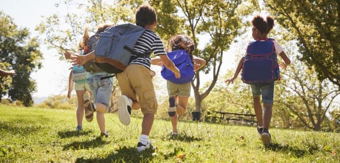 Five school kids running in a field, back view, close up